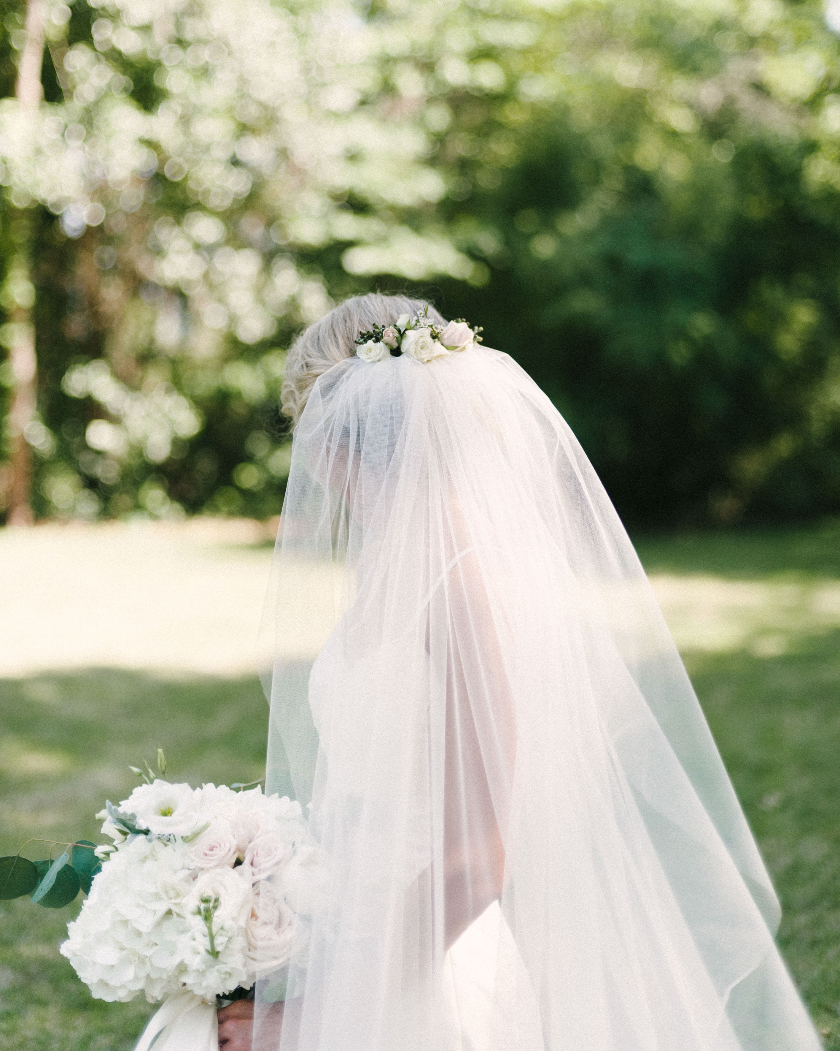 A super pretty backside image of bridal updo with floral veil in a lush green field located in Montgomery, AL
