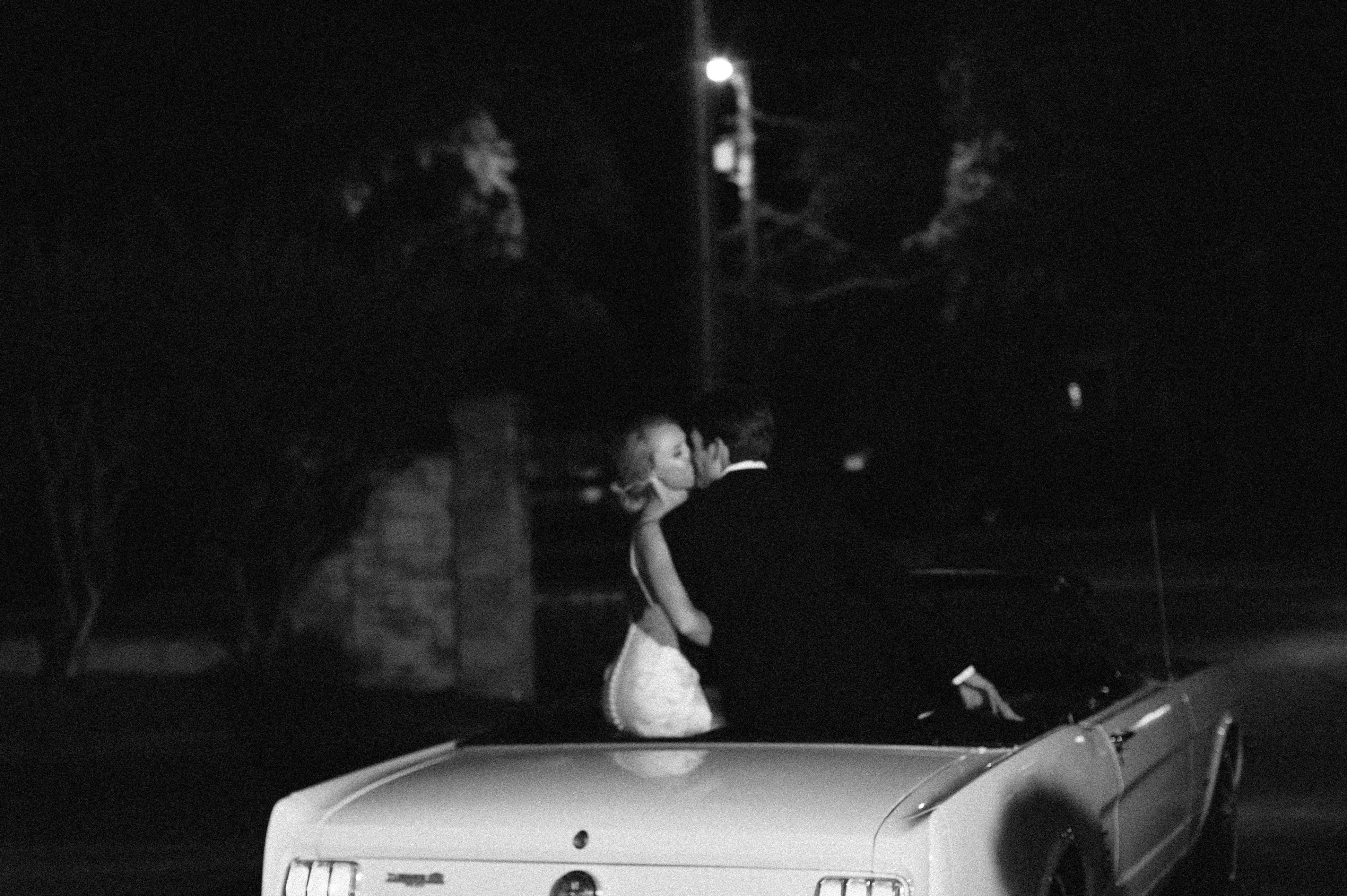 Bride and groom sendoff kissing while on top of a vintage convertible from Selma, Alabama wedding - ilford hp5 photo edit by Olivia Joy Photography