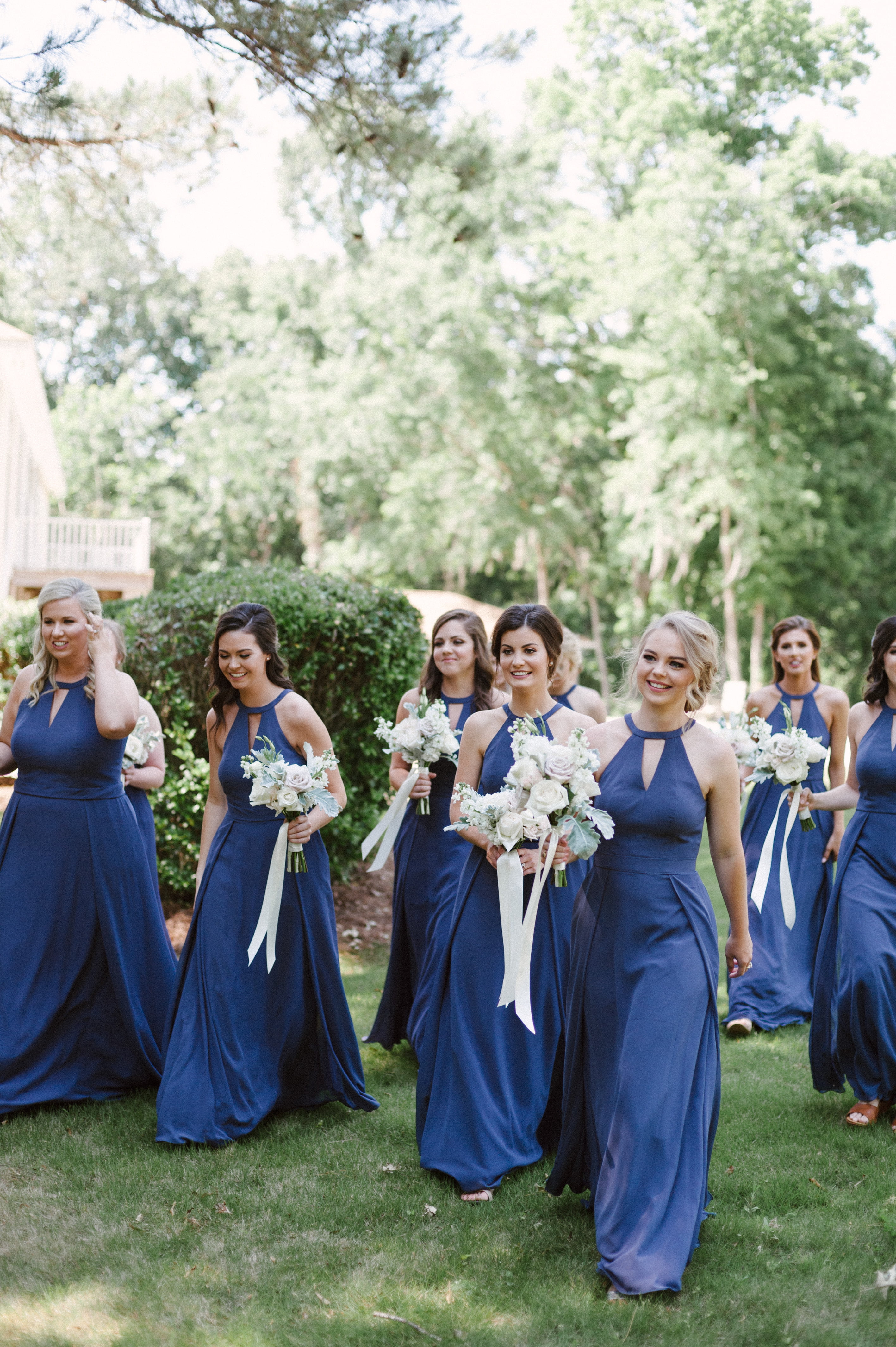 A super happy bridal party approaching a grassy landscape for wedding party photos in Selma, Alabama behind Swift Creek