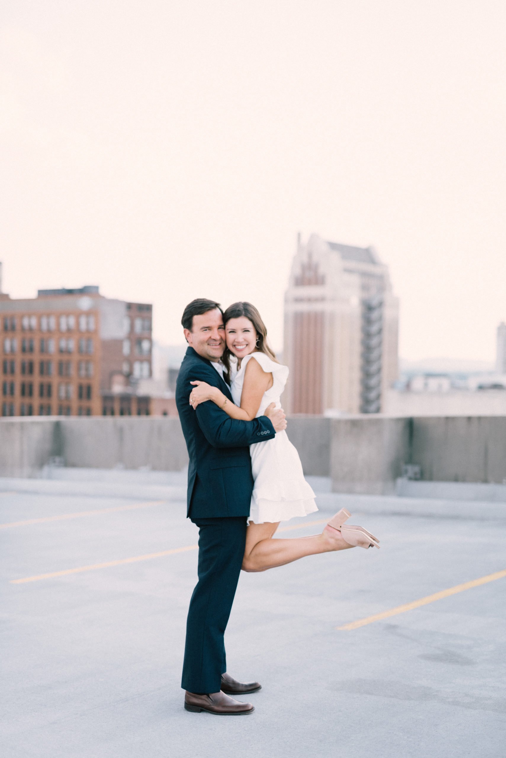 Excited engaged couple posing for their engagement session on a rooftop in downtown Birmingham AL