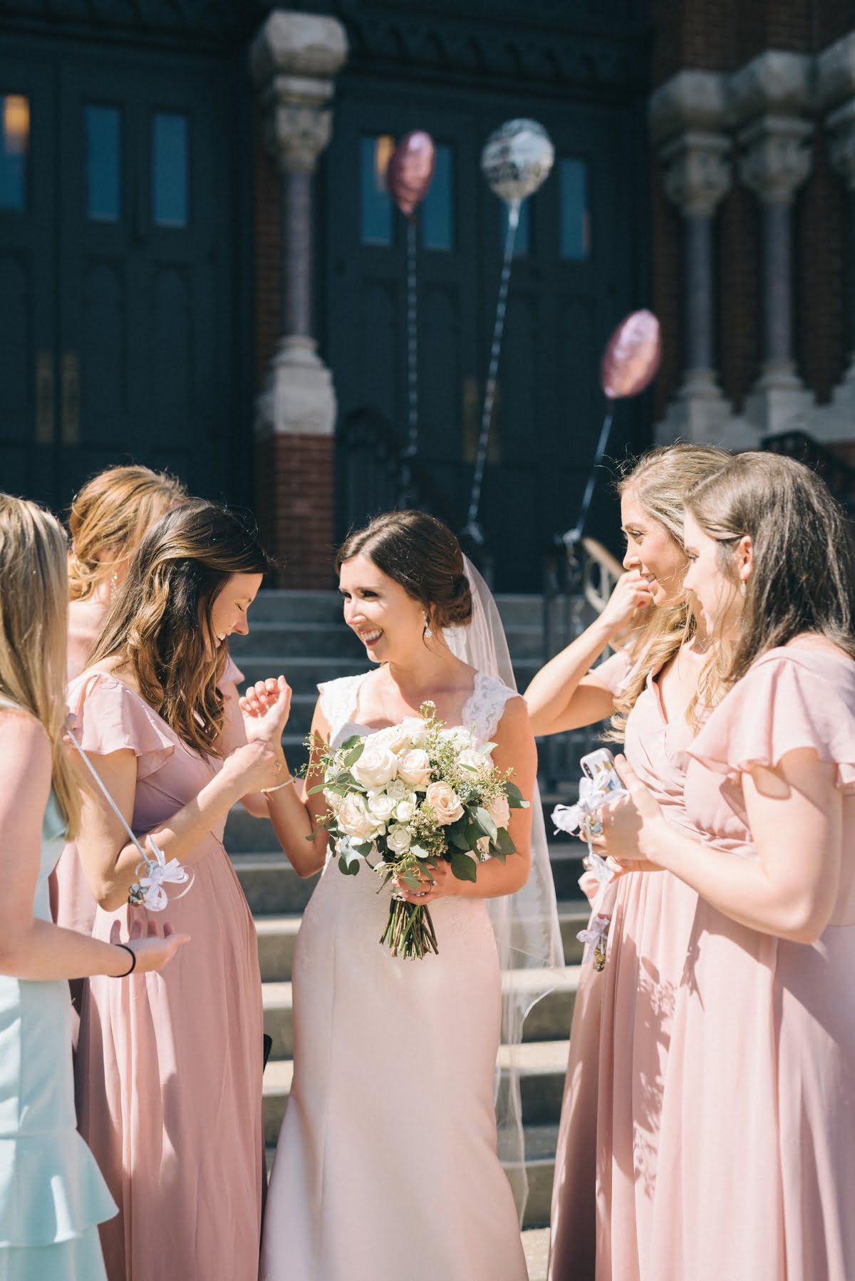 A candid image of joyful bridesmaids surrounding the bride who just got married in front of Cathedral of St Paul's Birmingham, AL