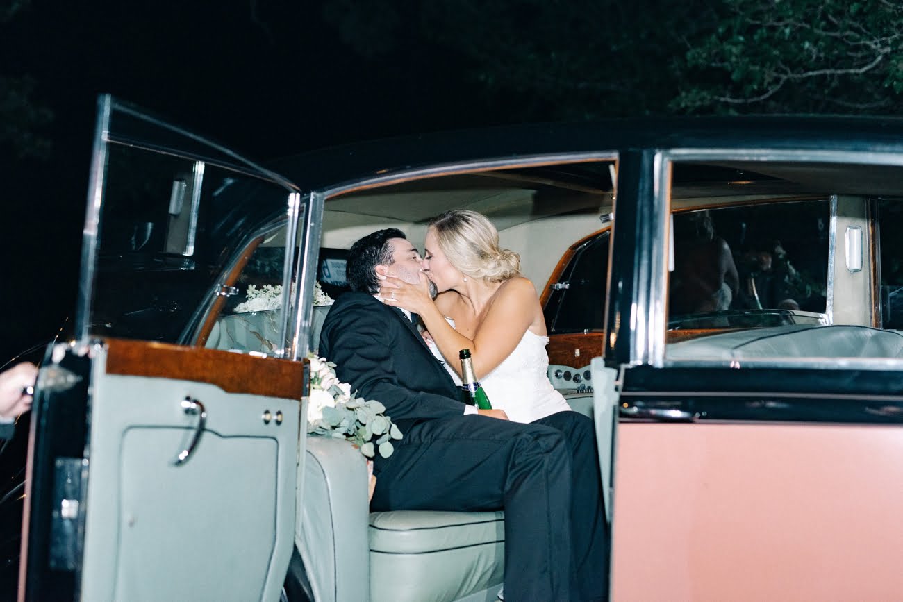 Super fun photo of newly married wedding couple in their vintage getaway car kissing before leaving for their honeymoon in Birmingham wedding venues of Alabama