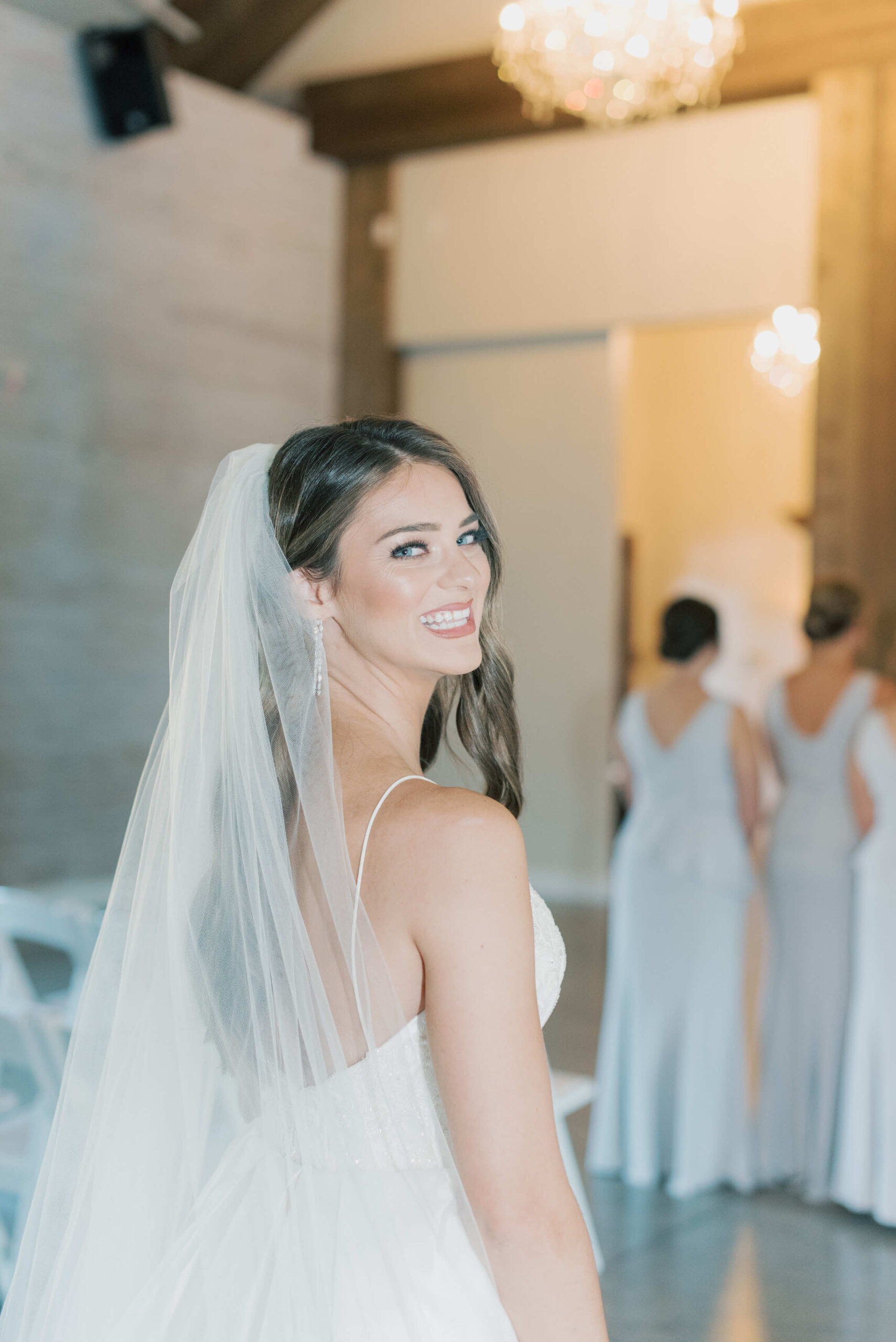 A bride smiling at the camera before her first look with her bridesmaids in the Carriage House facility of Park Crest wedding venue in Hoover, AL