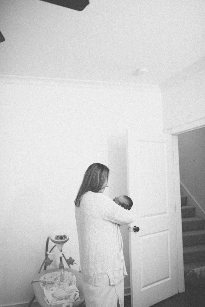 A mother carefully carrying her new baby boy out of a room in their house