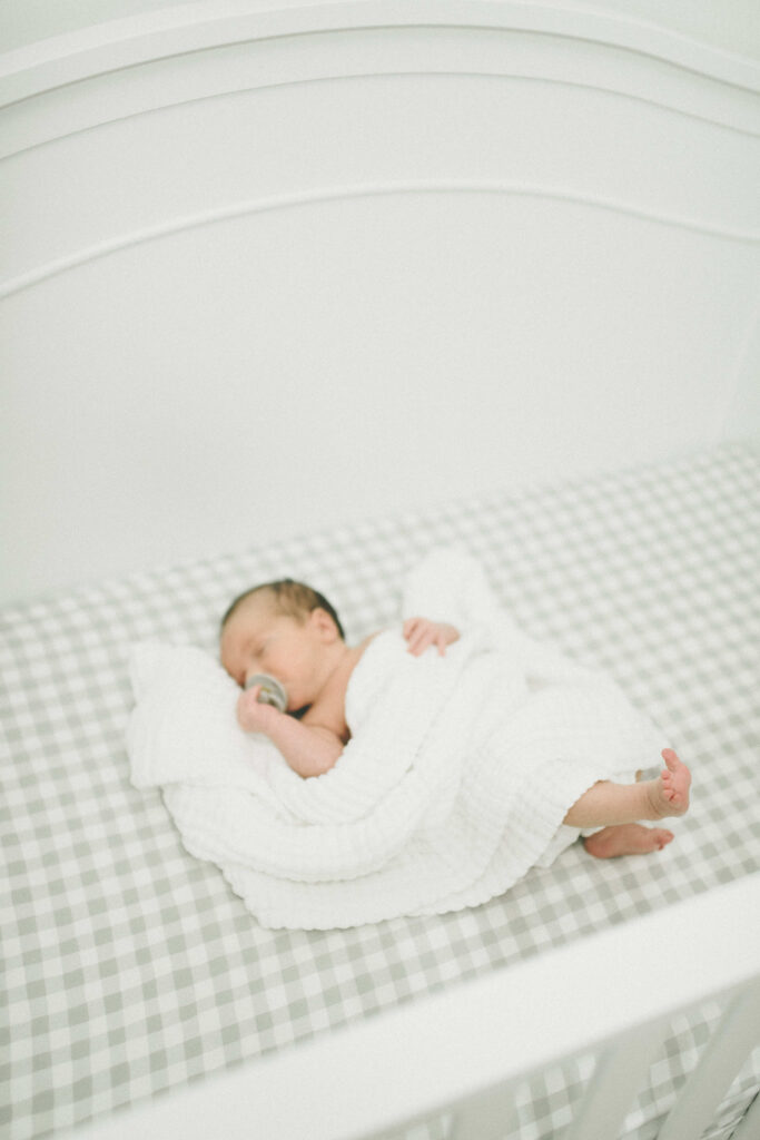 A baby boy in his crib with his little toes poking out of a gauze baby blanket