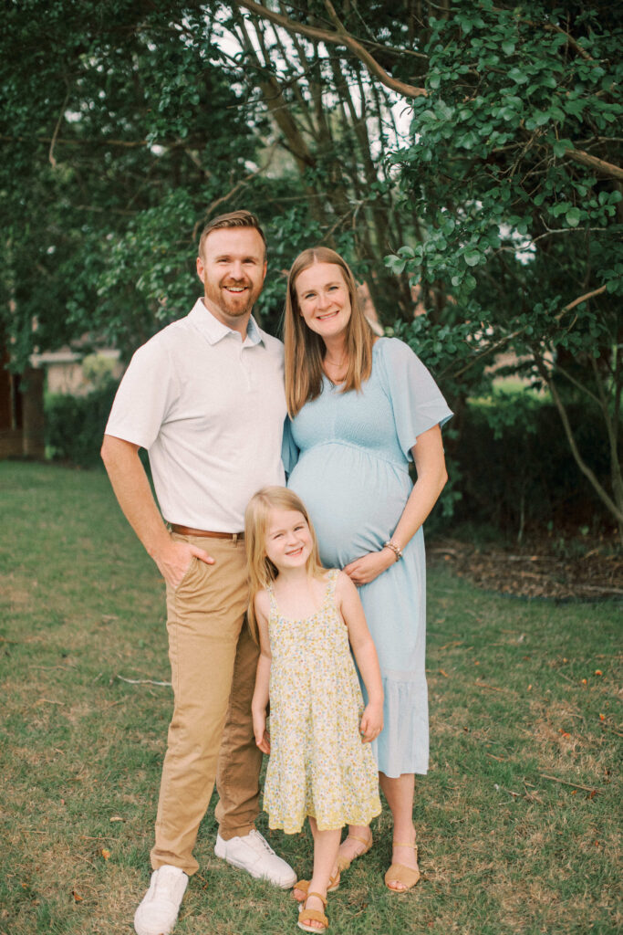 Family of three with daughter looking at camera smiling because they are happy they're expecting a baby. Maternity photos