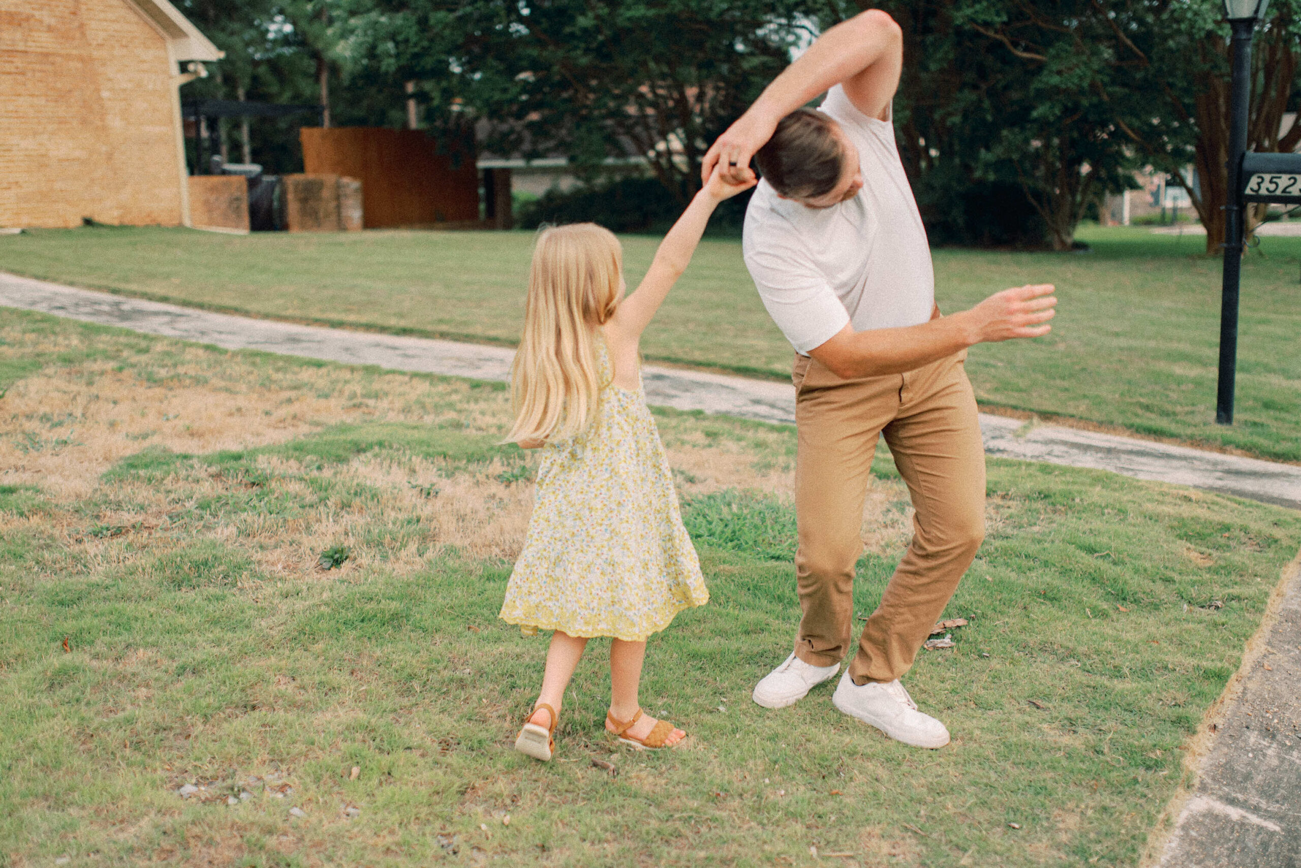 Dad being silly dancing with daughter dancing and twirling in front of their house in the yard