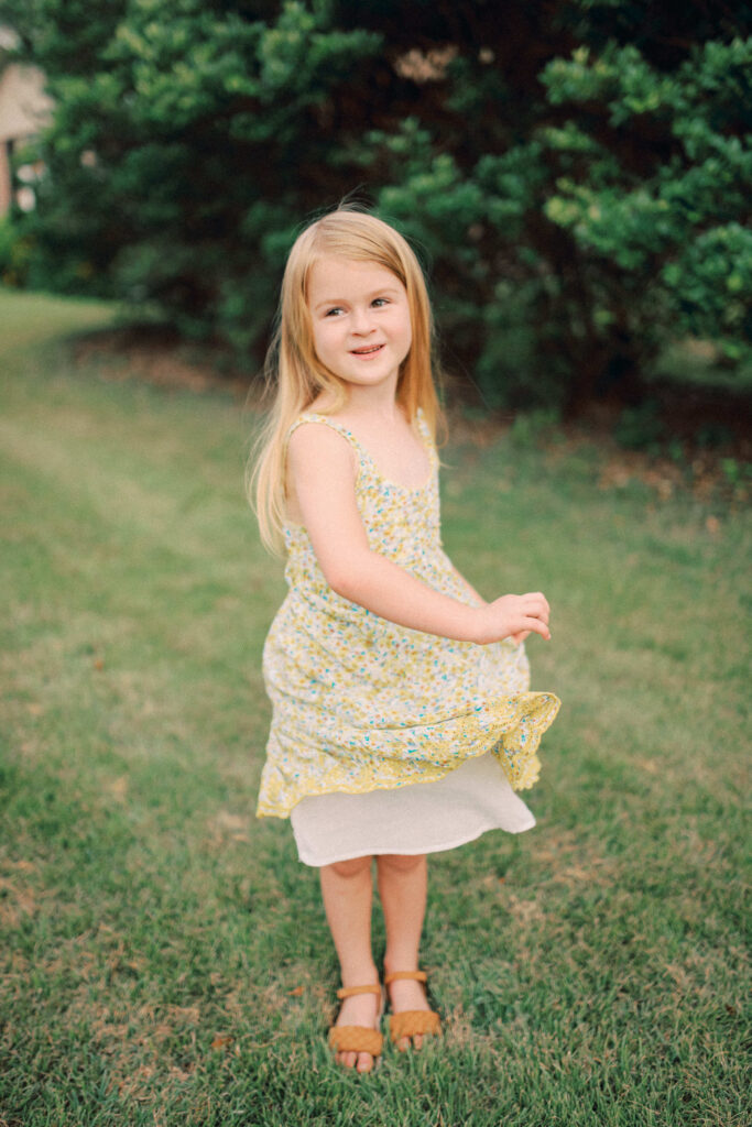 A portrait of a little girl outside twirling her dress while looking off to her mom and dad